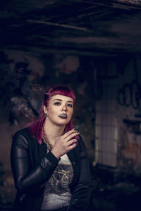 Portrait of young woman smoking cigarette while sitting in abandoned building