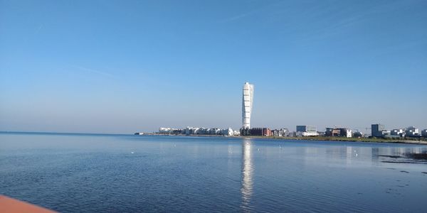 Sea by buildings against clear blue sky