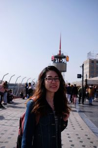 Portrait of young woman standing on street in city against clear sky