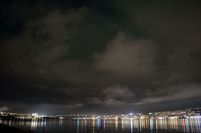 Illuminated harbor by sea against sky at night