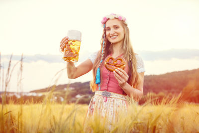 Portrait of a smiling young woman holding plant on field