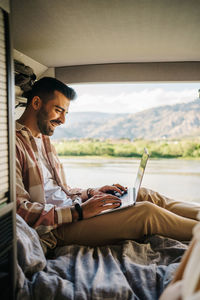 Content hispanic man working on laptop while sitting in camper during trip