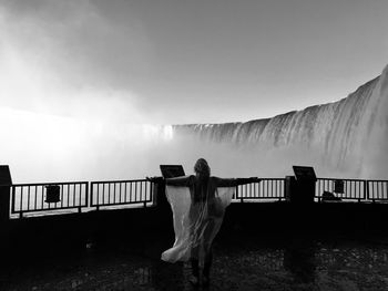 Rear view of woman standing on footbridge against sky