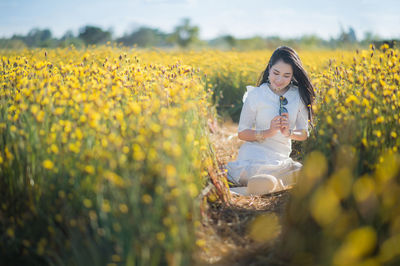 Woman sitting amidst yellow flowering plants on field