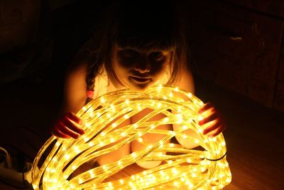 Portrait of cute girl holding illuminated lighting equipment in darkroom at home