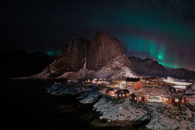 Illuminated buildings by mountain against sky at night