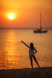 Rear view of woman standing in sea during sunset