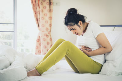 Woman with stomachache sitting on bed