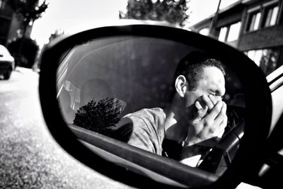 Young man with hands covering mouth reflecting on side-view mirror