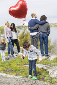 Boy holding balloon on rock with homosexual families in background
