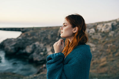 Young woman looking away while standing on rock