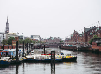 Boats moored at harbor by buildings in city against sky