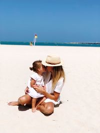 Mother and daughter kissing at beach against clear sky