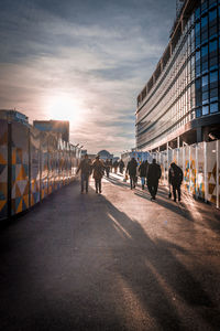 People walking on sidewalk in city against sky