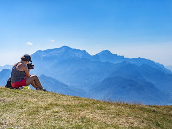 Woman sitting on mountain against sky