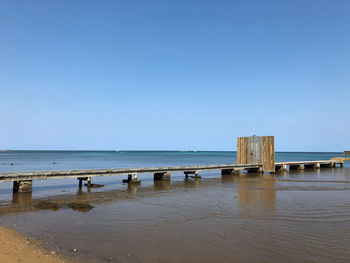 Pier over sea against clear blue sky