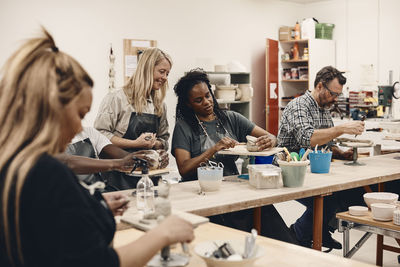 Woman discussing over clay with instructor while artists molding clay sitting at table in art class