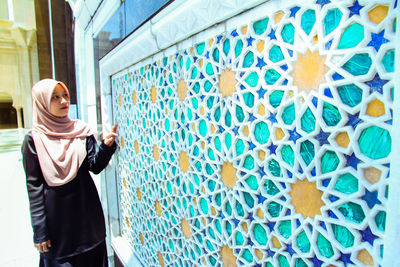 Woman wearing hijab while standing by patterned wall at mosque