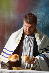 Man wearing scarf holding bread against wall at home