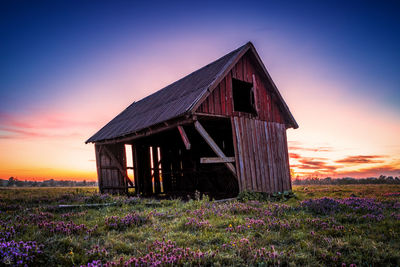 Old wooden house on field against sky during sunset