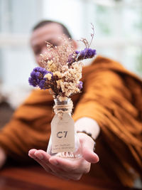 Close-up of monk holding flower in bottle outdoors