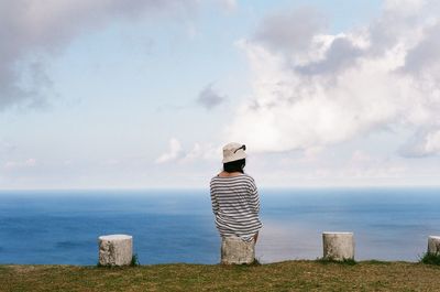 Rear view of woman sitting on post against sea 