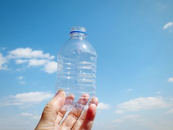 Close-up of hand holding plastic bottle against sky