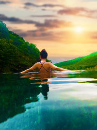 Rear view of woman relaxing in infinity pool during sunset