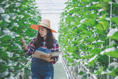 Young woman wearing hat standing against plants