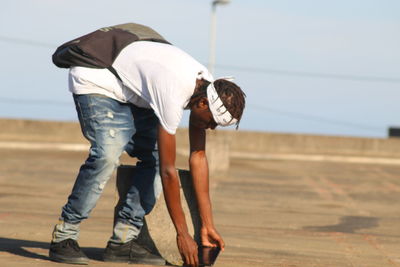 Side view of young man bending while standing on footpath