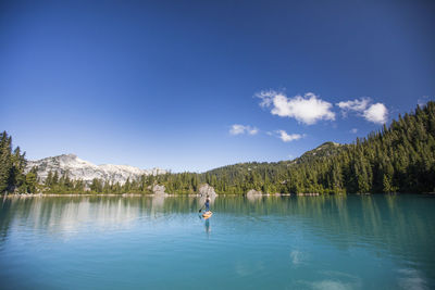 Fit woman paddles stand up paddle board on blue lake.