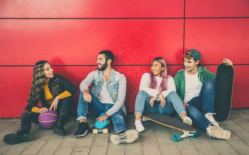 Full length of young couple sitting against wall