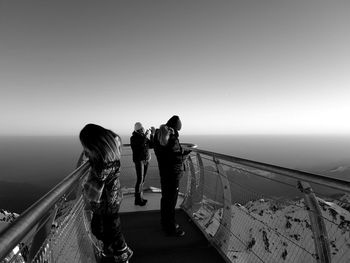 People standing by railing against sea and clear sky