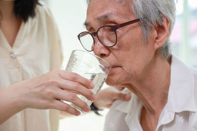 Midsection of nurse feeding water to senior woman