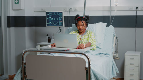 Young woman using laptop on bed at hospital