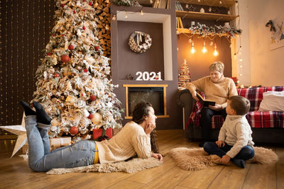 Grandmother telling story to grandchildren by christmas tree at home