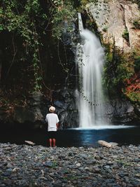 Rear view of man looking at waterfall in forest