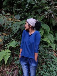 Young man looking away while standing against plants