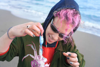 Smiling woman with dyed hair holding dead crab at beach