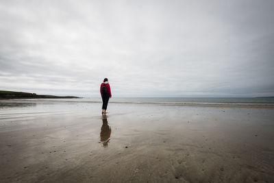 Rear view of woman standing on beach against sky