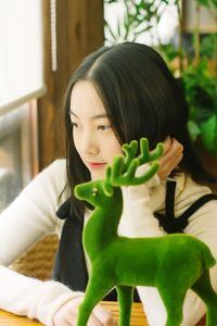 Thoughtful young woman sitting by green deer figurine at table