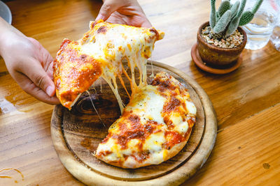 High angle view of hand holding pizza on table