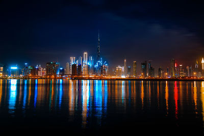 Illuminated buildings by river against sky at night