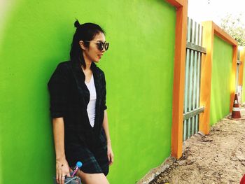 Woman in sunglasses standing against green wall