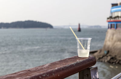 Close-up of plastic cup with cold beverage on wooden railing