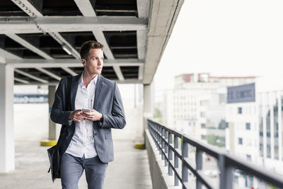 Young businessman using smartphone, walking on parking level