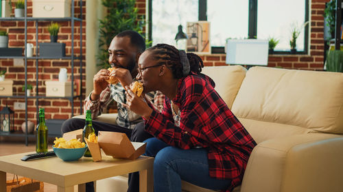 Smiling friends using phone while sitting on sofa at home