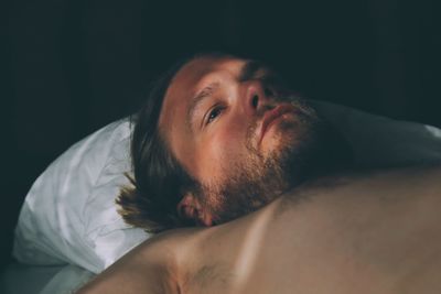 Close-up of thoughtful shirtless man looking away while lying down on bed