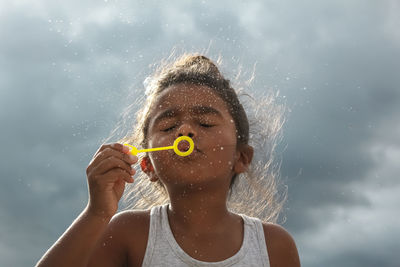 Close-up of girl blowing on bubble wand against sky