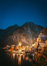 Illuminated buildings by mountains against sky at night